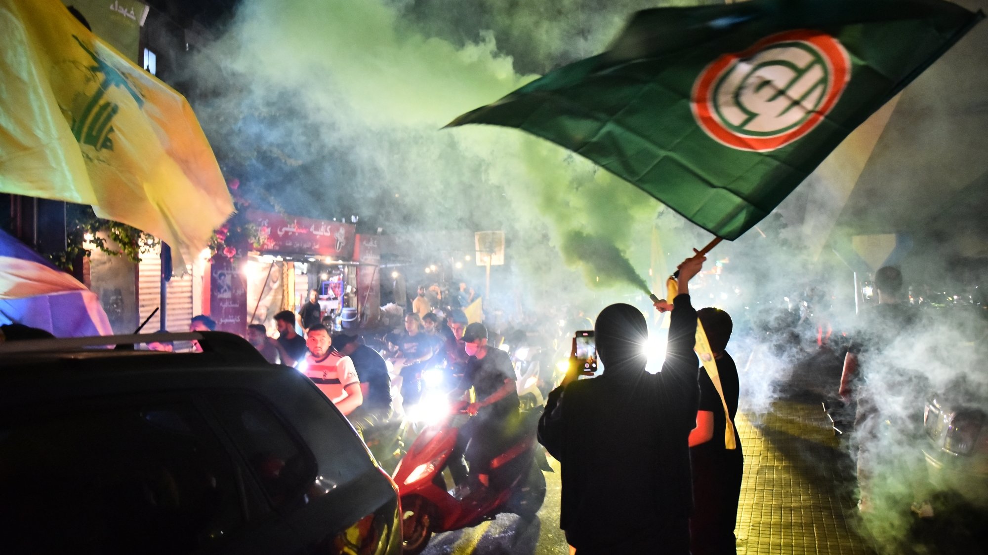 Des manifestants brandissent des drapeaux sous une fumée colorée dans une ambiance festive.