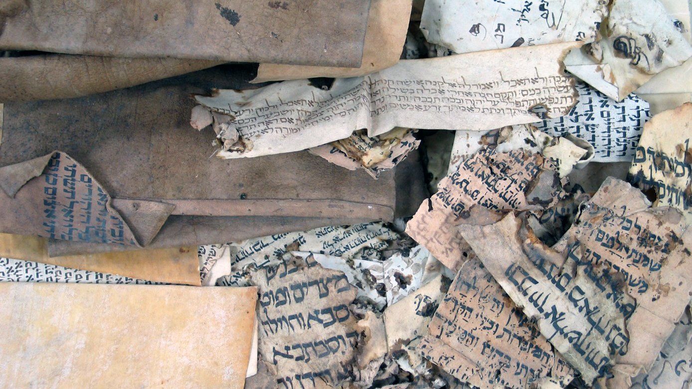 L'image montre un ensemble de vieux manuscrits et de documents enroulés et usés. Les pages sont usées, certaines sont jaunies et déchirées, et on peut voir des inscriptions écrites dans des langues anciennes et probablement des alphabets différents. La texture des papiers varie, certains étant plus épais que d'autres, et la composition générale donne une impression d'antiquité et de fragilité, suggérant leur importance historique.