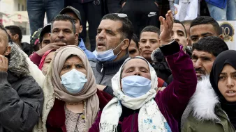 L'image montre une foule de personnes, principalement des hommes et des femmes, réunies pour exprimer leurs émotions. Certaines personnes portent des masques faciaux, et il y a des expressions de détermination et de protestation parmi les membres du groupe. Les vêtements sont variés, avec des accents de couleurs différentes. L'ambiance semble animée et engagée, suggérant une manifestation ou un rassemblement pour une cause.