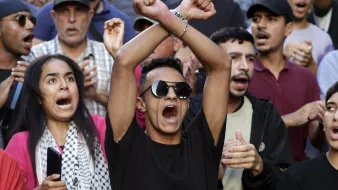 Groupe de manifestants exprimant des émotions fortes, certains brandissant les bras.