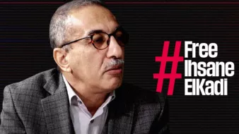 L'image montre un homme portant des lunettes et un costume à carreaux. Il semble participer à une interview ou à un débat, étant tourné vers un interlocuteur. À côté de lui, le texte en gras indique "#Free Ihsane ElKadi", suggérant qu'il est lié à une campagne de sensibilisation ou de soutien pour cette personne. L'arrière-plan présente un design graphique sobre, probablement pour mettre en avant le message.