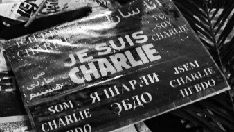 L'image montre une affiche ou un panneau avec l'inscription "JE SUIS CHARLIE" en plusieurs langues. Les mots sont écrits en noir sur fond blanc, et le tout a un aspect qui évoque le soutien et la solidarité, probablement en rapport avec les événements tragiques auxquels cette phrase fait allusion. On peut également voir des éléments environnants qui semblent être des morceaux de papier ou des affiches, ce qui donne un aspect de rassemblement ou de manifestation.