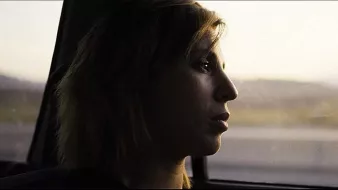 L'image montre une silhouette d'une personne assise à l'intérieur d'une voiture. Elle regarde par la fenêtre, prenant un moment de réflexion. La lumière est douce, créant une ambiance mélancolique, et le paysage flou en arrière-plan suggère un voyage en cours. Le visage de la personne est partiellement éclairé, mettant en valeur une expression pensante.