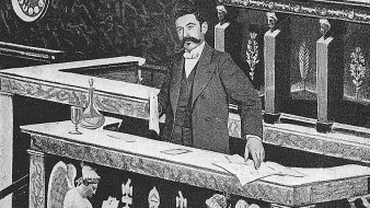 L'image montre un homme bien habillé, debout derrière un bureau ou une table qui semble faire partie d'une institution, probablement un parlement ou une assemblée. Le bureau est décoré avec des motifs ornementaux et des sculptures d'anges de chaque côté. L'homme semble concentré, tenant des documents, et l'ambiance générale est formelle et historique.