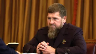 Homme avec une barbe, vêtu d'un costume sombre, assis à une table.