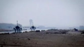 L'image montre deux avions militaires aperçus au loin dans un paysage désertique. L'atmosphère est légèrement brumeuse, ce qui donne une impression de profondeur. On peut distinguer une piste d'atterrissage ou d'envol, et le sol semble aride avec peu de végétation. Les avions sont visibles, mais les détails sont flous en raison de la distance et de la qualité de la prise de vue.