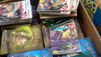 L'image montre une boîte remplie de livres empilés les uns sur les autres. On peut apercevoir différents titres en arabe sur les couvertures, illustrés par des images colorées. Certains livres semblent appartenir à des séries de contes ou de romans graphiques, avec des illustrations captivantes et des textes en arabe. L'ensemble donne une impression d'abondance littéraire.