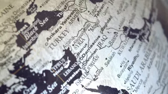 L'image montre une carte en noir et blanc d'une région qui inclut le Moyen-Orient et certaines parties de l'Europe et de l'Asie. On peut distinguer des pays comme la Turquie, l'Iran, l'Irak et l'Arabie Saoudite. Les noms des villes et des pays sont inscrits en lettres claires, créant un contraste avec le fond noir. La carte semble stylisée, donnant une impression de vintage ou d'art graphique.