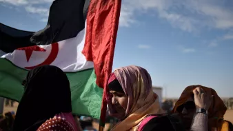 Des femmes portant une écharpe colorée et une grande bannière. Ciel dégagé en arrière-plan.