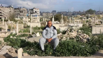 Un homme assis parmi des tombes dans un cimetière, entouré de végétation.