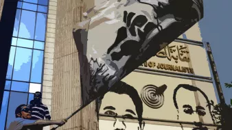 L'image montre un homme en train de brandir un grand drapeau devant un bâtiment qui semble être un bureau de presse. En arrière-plan, on peut voir des portraits d'hommes peints sur le mur de l'immeuble. Le décor donne une impression de manifestation ou de soutien, et une partie du texte sur le bâtiment est écrite en arabe. Les expressions des figures représentées semblent sérieuses, ajoutant à l'ambiance de l'image.