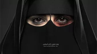 L'image montre une femme portant un niqab, couvrant la majeure partie de son visage. Ses yeux sont mis en valeur, l'un d'eux ayant un maquillage sombre, tandis que l'autre semble plus clair. Cette composition crée un contraste saisissant. En bas de l'image, il y a un texte en arabe et le logo de la Fondation King Khalid. L'image semble porter un message puissant et engageant.