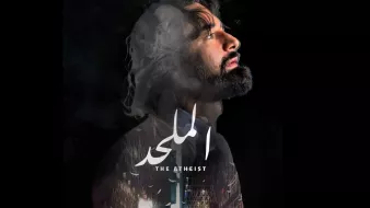 L'image semble représenter une affiche de film intitulée "The Atheist" ou "الملاحد". On y voit un homme avec une expression introspective, le regard tourné vers le haut, entouré de fumée ou de nuages, ce qui crée une ambiance mystérieuse. En arrière-plan, il y a des éléments architecturaux ou urbains. Le titre du film est centré et bien en évidence, avec des informations sur le réalisateur et l'auteur en bas. L'ensemble dégage une atmosphère dramatique et contemplative.