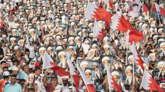 L'image montre une grande foule de manifestants réunis, brandissant des drapeaux et des portraits. Les personnes sont vêtues de manière variée, certaines portant des keffiehs. Les drapeaux représentent probablement le pays en question, tandis que les portraits semblent être ceux de figures clés ou de leaders. L'atmosphère dégage une forte impression de solidarité et de mobilisation autour d'une cause politique ou sociale.