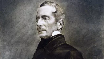 L'image montre un portrait en noir et blanc d'un homme d'âge moyen, vêtu d'un manteau sombre. Son expression est sérieuse et réfléchie, avec des traits du visage bien définis. Il a les cheveux légèrement ondulés, peignés vers l'arrière, et il porte un col montant. L'arrière-plan est flou, mettant en valeur le sujet du portrait. L'ensemble a un aspect classique et intemporel, caractéristique des portraits du 19ème siècle.