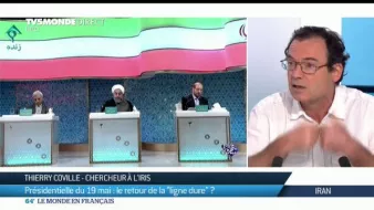 L'image présente une scène de débat ou de discussion, probablement liée à la politique. Au centre de l'image, on voit Thierry Coville, chercheur à l'IRIS, qui s'exprime avec des gestes. Derrière lui, trois personnes sont assises, dont l'une porte un costume clair. Le contexte semble lié à une élection présidentielle, évoquant des thèmes tels que la "ligne dure". L'image reflète un moment d'échange d'idées sur des enjeux politiques.