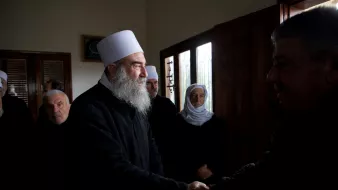 Des hommes en vêtements sombres se serrent la main dans une pièce avec des fenêtres.