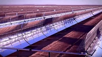 L'image montre un paysage d'énergie solaire, probablement un champ de miroirs ou de panneaux solaires. On peut voir plusieurs lignes de miroirs courbés, orientés vers le soleil. Ces miroirs concentrent les rayons solaires pour produire de l'énergie. L'arrière-plan est désertique ou plat, suggérant que l'installation est située dans une région ensoleillée. L'ambiance générale évoque une technologie moderne et des initiatives en faveur des énergies renouvelables.