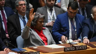 L'image montre une réunion au Conseil de sécurité des Nations Unies. Une femme, manifestement représentant les États-Unis, est assise à une table, levant la main pour prendre la parole ou voter. À côté d'elle, on aperçoit d'autres délégués de différents pays, tous attentifs. L'atmosphère semble sérieuse et concentrée, typique des discussions diplomatiques importantes.