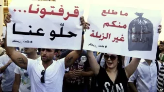 L'image montre une manifestation où des personnes tiennent des pancartes. Les messages sur les pancartes évoquent des revendications concernant la situation dans leur pays. L'une des pancartes semble exprimer un mécontentement face à la gestion des déchets, tandis que l'autre parle d'un désir de changement ou d'amélioration. Les manifestants semblent passionnés et engagés dans leur lutte. L'ambiance générale suggère une mobilisation citoyenne.