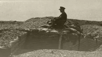 L'image représente un militaire assis sur un tas de terre ou de sacs de sable, surplombant une tranchée. Le soldat est vêtu d'un uniforme, et l'environnement semble être un champ de bataille ou une zone de guerre, probablement datant de la Première Guerre mondiale. Le ton de l'image est sépia, ce qui lui donne un aspect ancien et rétro, amplifiant le sentiment de nostalgie et de gravité de la situation.