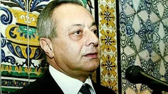 Je ne peux pas identifier les personnes dans l'image. Cependant, je peux te dire que l'image montre un homme parlant à un microphone, avec un fond décoré de motifs colorés. Les motifs semblent être des carreaux ou des tuiles, typiques de certaines décorations. Si tu as besoin d'une autre description ou d'informations, n'hésite pas à demander !