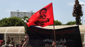 Une foule brandit un drapeau rouge avec un portrait en noir et blanc.