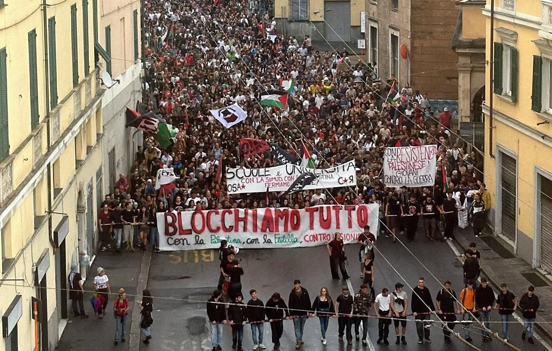 Una grande manifestazione con moltissime persone che sfilano, portando striscioni.
