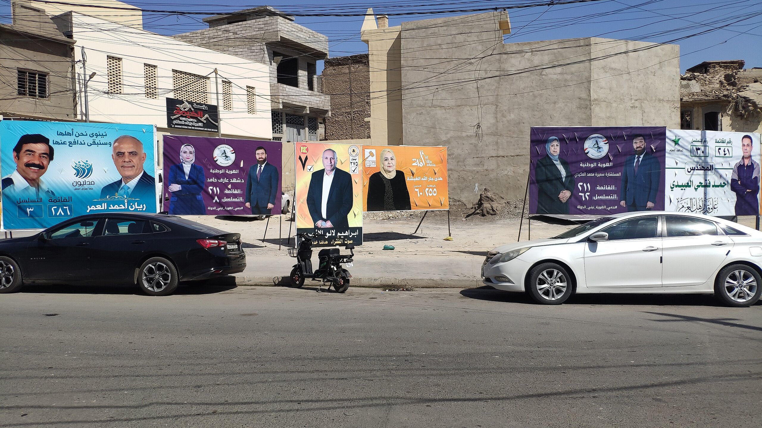 Una strada con diversi manifesti pubblicitari colorati su un muro di fondo.