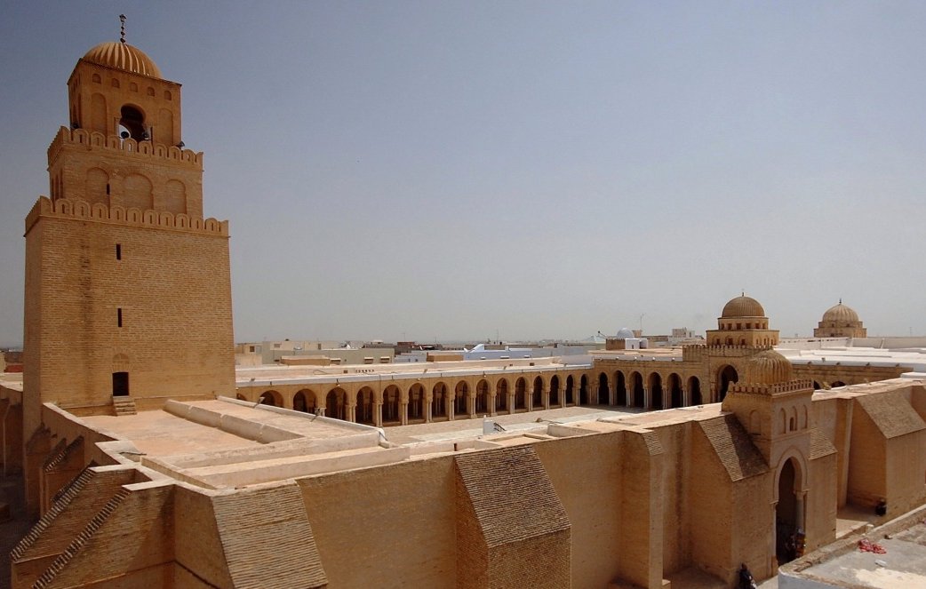 Edificio storico con torri e architettura in sabbia chiara, sole intenso.