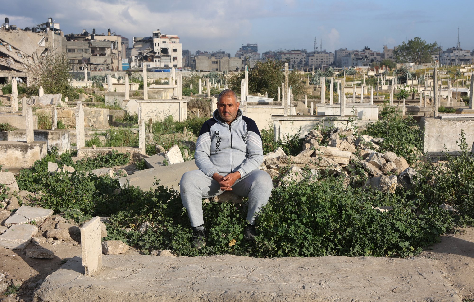 Un uomo seduto in un cimitero, circondato da tombe e vegetazione.