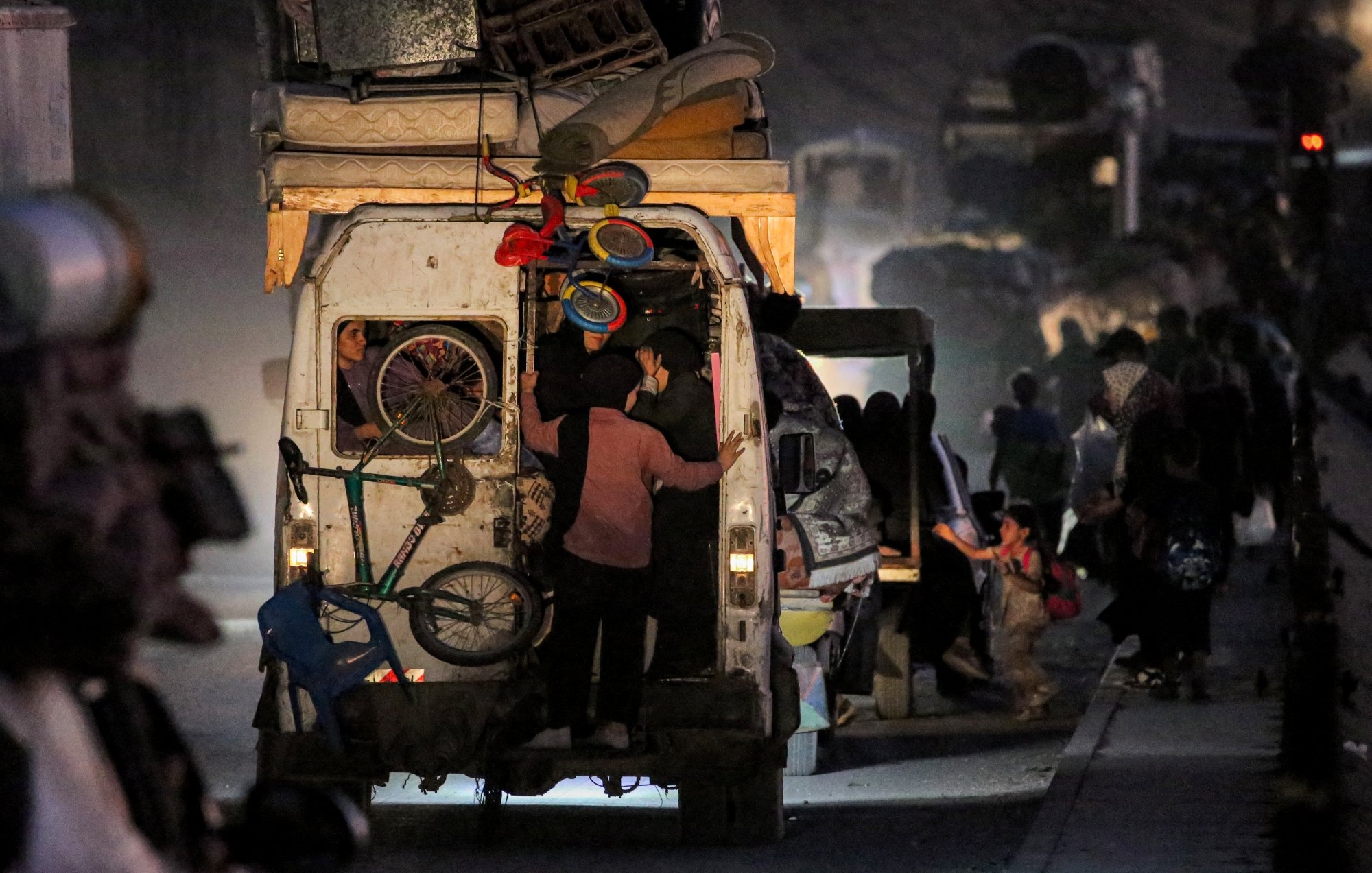 Un furgone pieno di oggetti, persone in movimento in un ambiente polveroso e notturno.