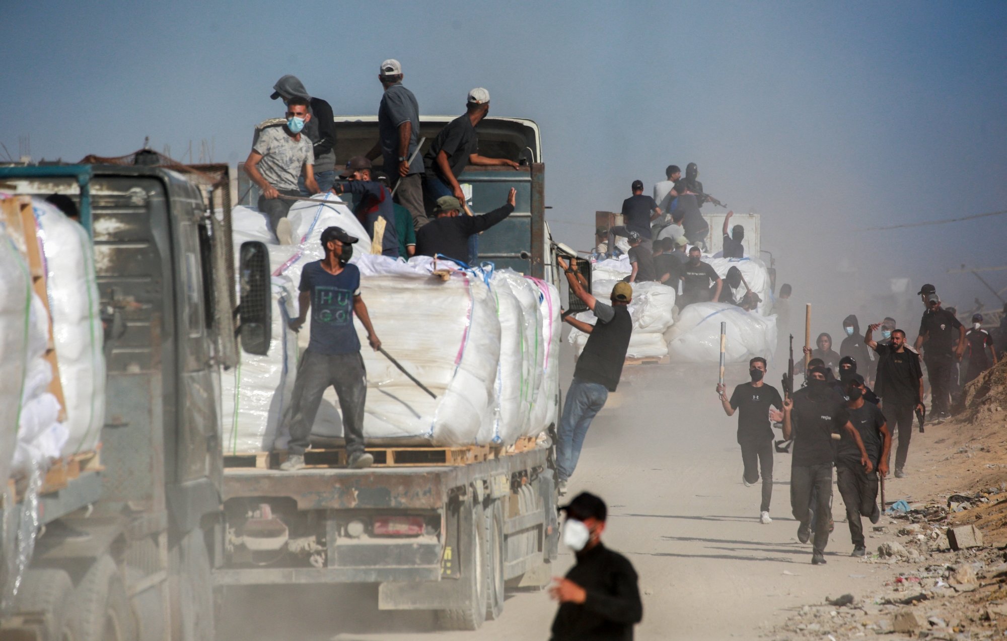 Un gruppo di persone lavora attorno a camion in una zona polverosa.