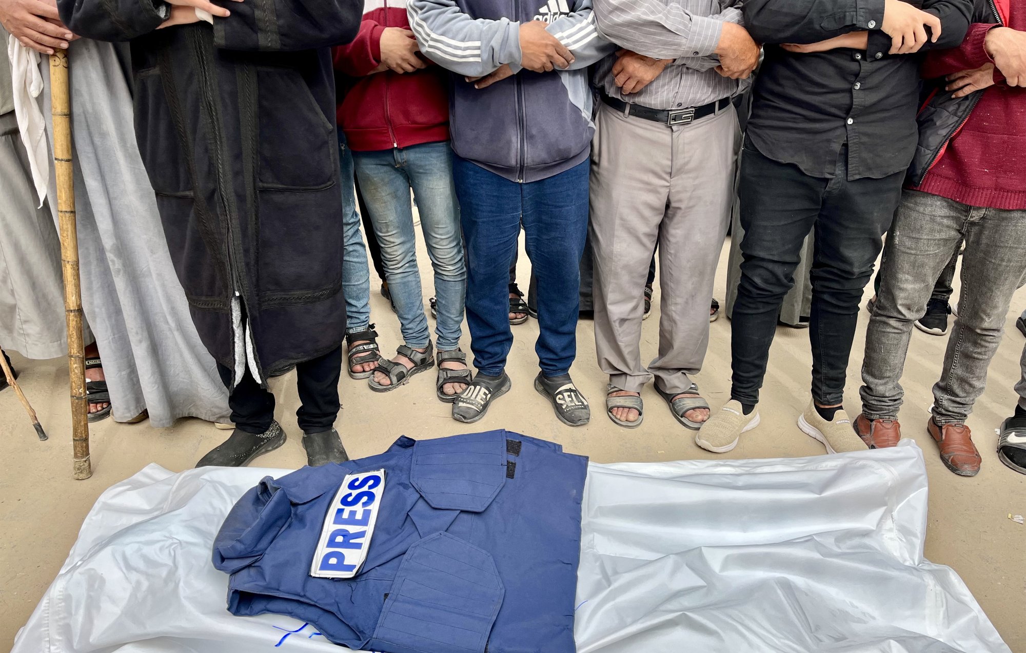 Gruppo di persone in piedi attorno a una giacca con scritto "PRESS" su un telo.
