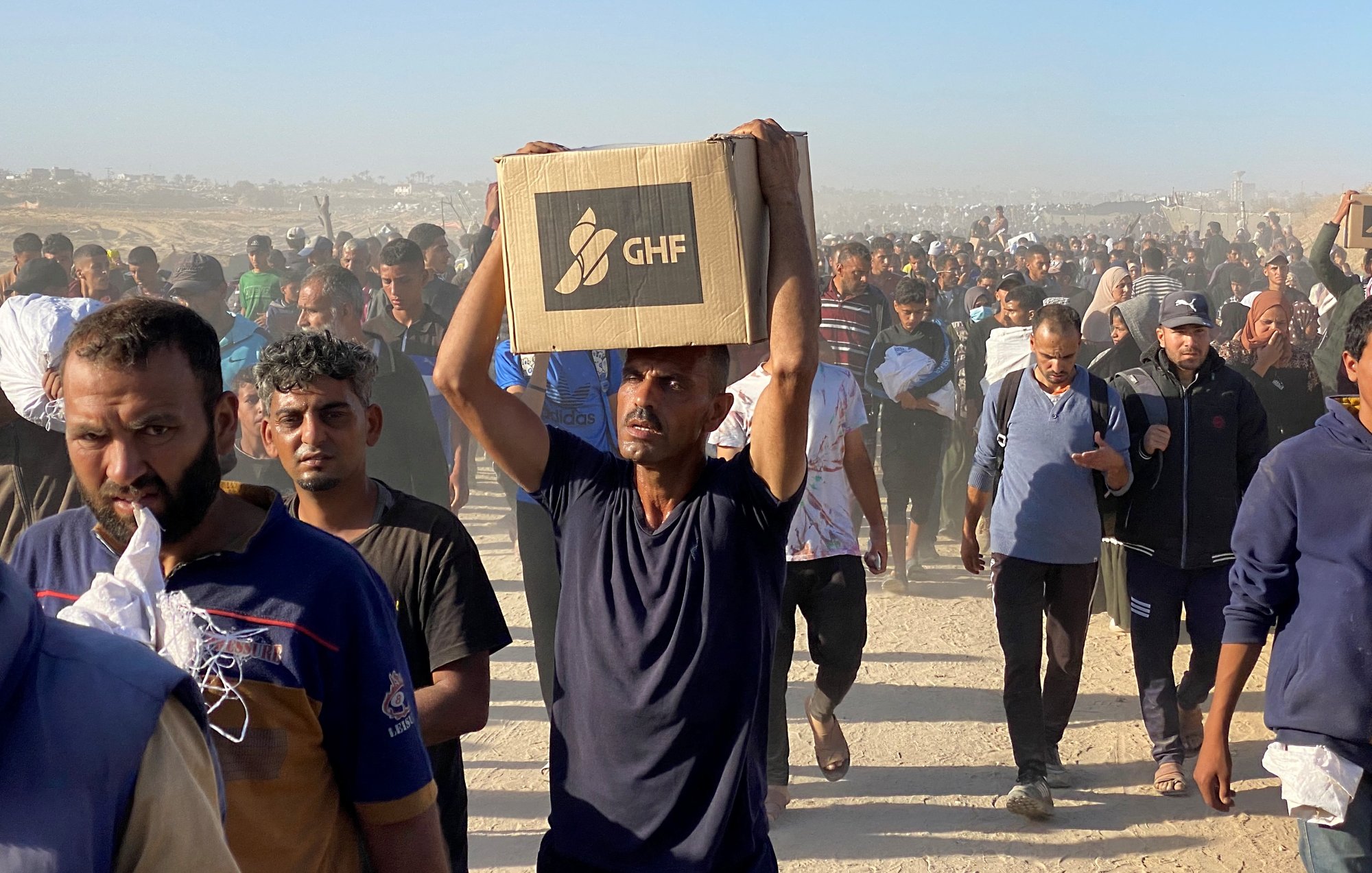 Un gruppo di persone cammina in un ambiente polveroso, portando scatole.