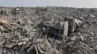 L'immagine mostra un vasto paesaggio di distruzione, con edifici in rovina e detriti sparsi ovunque. Ci sono strutture crollate e macerie che si estendono fino all'orizzonte, creando un'atmosfera di desolazione e abbandono.