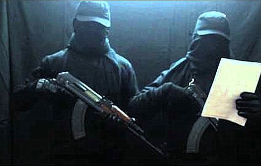 L'image montre deux individus habillés en noir, portant des masques et des casquettes. Ils tiennent des armes à feu, et l'un d'eux tient aussi un document. L'arrière-plan est sombre, ce qui accentue l'atmosphère mystérieuse de la scène.