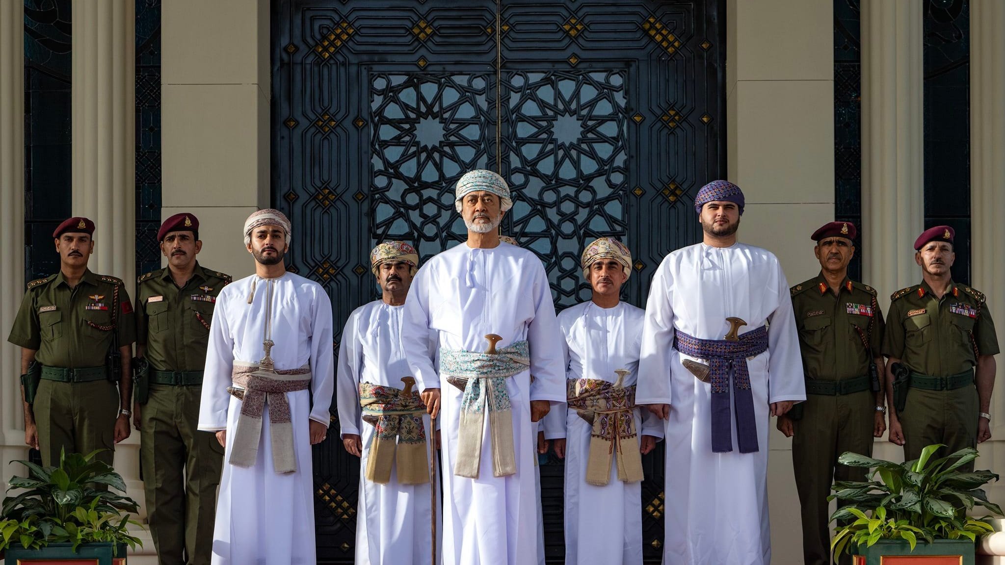 Groupe en tenues traditionnelles, debout devant un bâtiment orné, entouré de gardes.