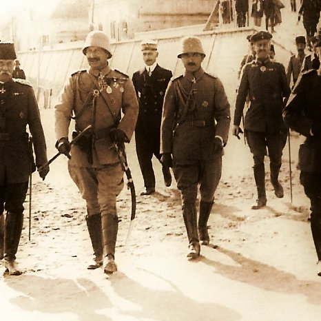 این تصویر قدیمی گروهی از افسران نظامی را نشان می‌دهد که در حال راه رفتن در یک منطقه بیرونی هستند. افراد به پوشش‌های نظامی با مدال‌ها و نشانه‌های متفاوت بر تن دارند. فضای اطراف ناآشکار است، اما به نظر می‌رسد که در یک رویداد رسمی یا نظامی حضور دارند. علاوه بر افسران، چند نفر دیگر نیز در پس‌زمینه دیده می‌شوند که ممکن است از مقام‌های دیگر یا مهمانان ویژه باشند. تصویر به صورت سیاه و سفید ثبت شده و حسی تاریخی دارد.