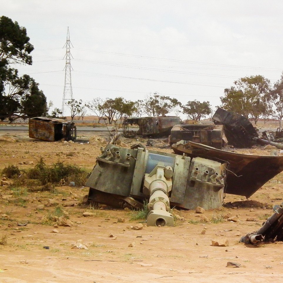 تظهر في الصورة مجموعة من الآليات العسكرية المدمرة والمستخرجة في منطقة صحراوية. تتناثر بقايا الدبابات والمعدات في بيئة جافة، مع بعض الأشجار القليلة في الخلفية. السماء ملبدة بالغيوم، مما يعطي إحساسًا بالوحدة والخراب للمكان. الكهربائية متواجدة في الخلفية، مما يشير إلى وجود بنية تحتية قريبة، ولكنها تبدو بعيدة عن هذه الفوضى.