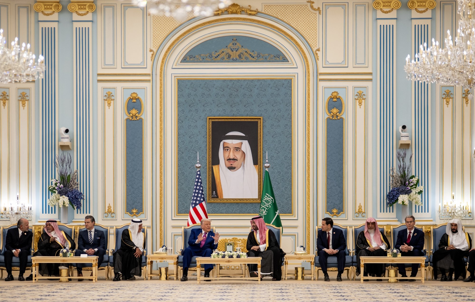 A formal meeting with leaders seated in an ornate room, a large portrait on the wall.