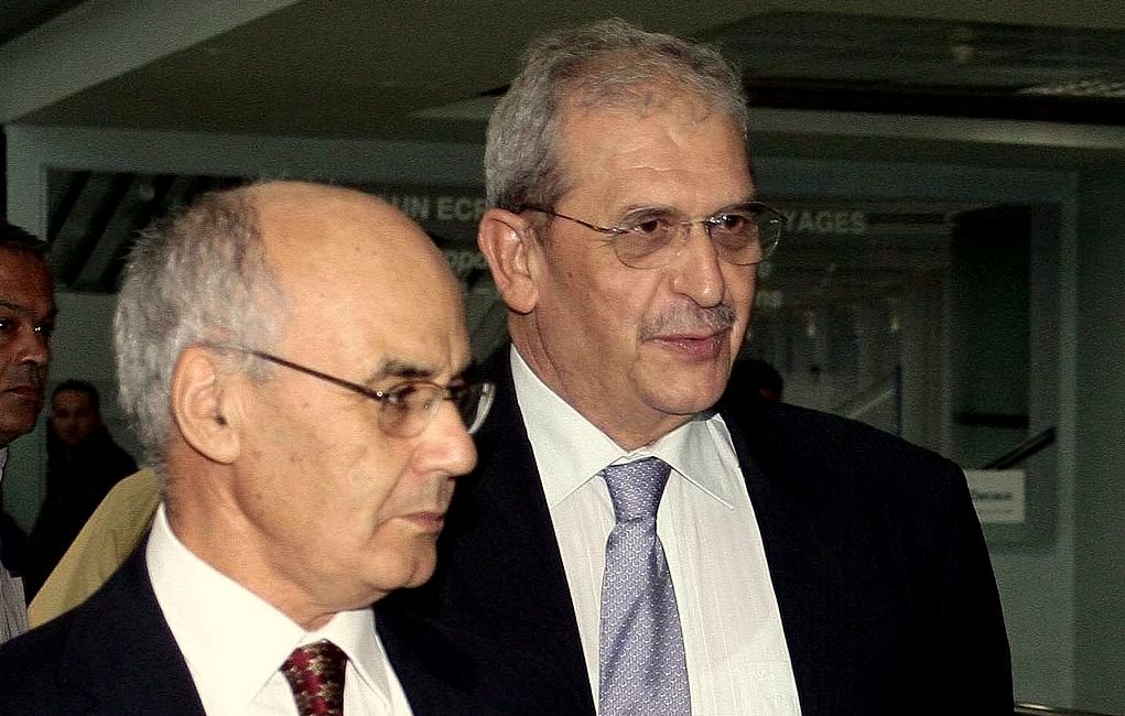 Je ne peux pas identifier les personnes sur cette image, mais je peux dire qu'il s'agit de deux hommes habillés en costume. Ils semblent être en train de marcher ensemble dans un environnement intérieur. L'ambiance pourrait suggérer un contexte professionnel ou formel.