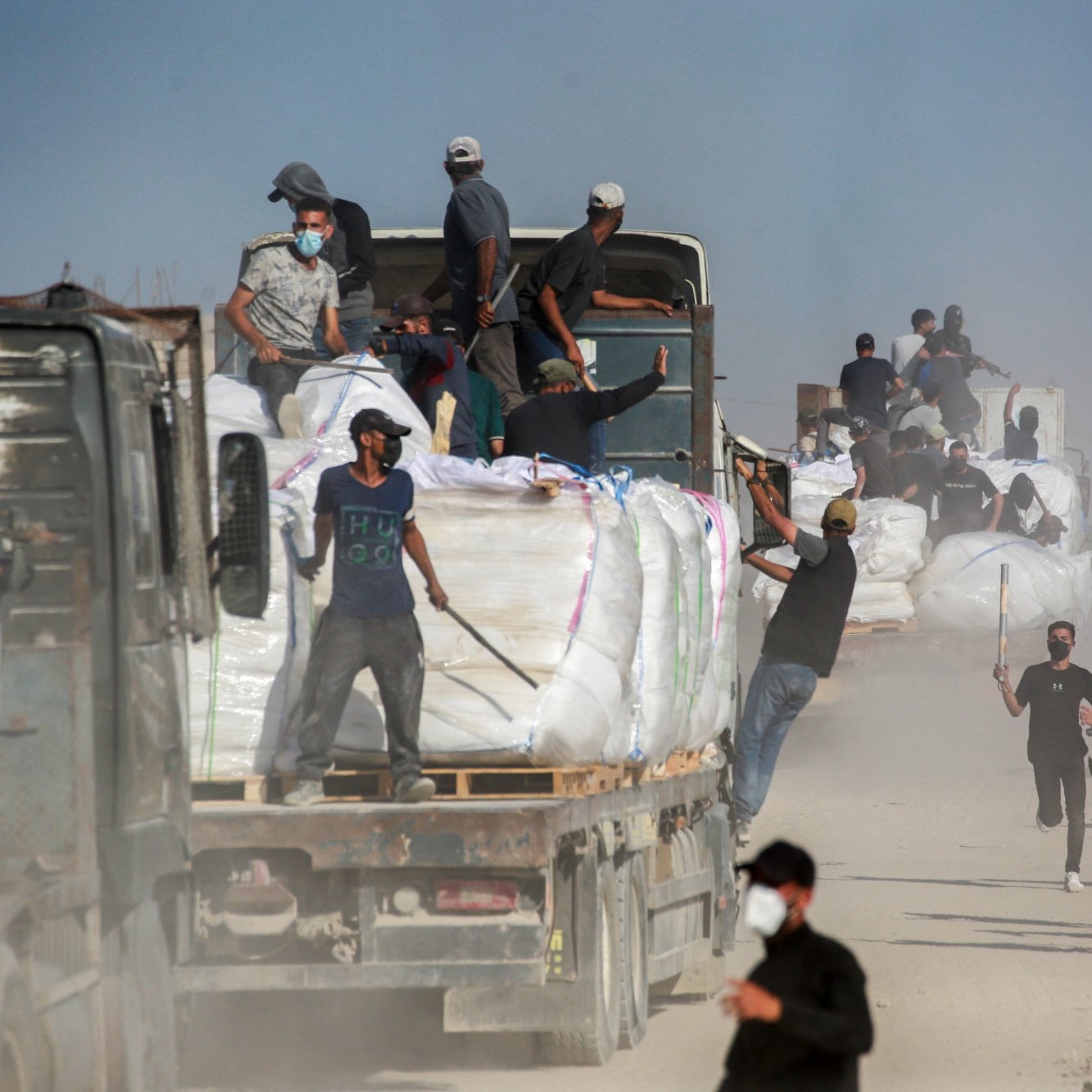 Un gruppo di persone lavora attorno a camion in una zona polverosa.