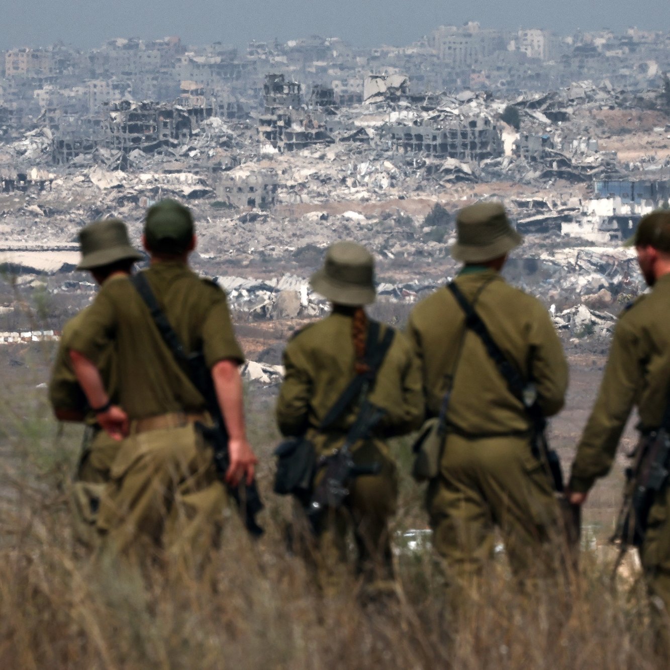 گروهی از سربازان با لباس نظامی به سمت یک منطقه ویران و تخریب‌شده نگاه می‌کنند.
