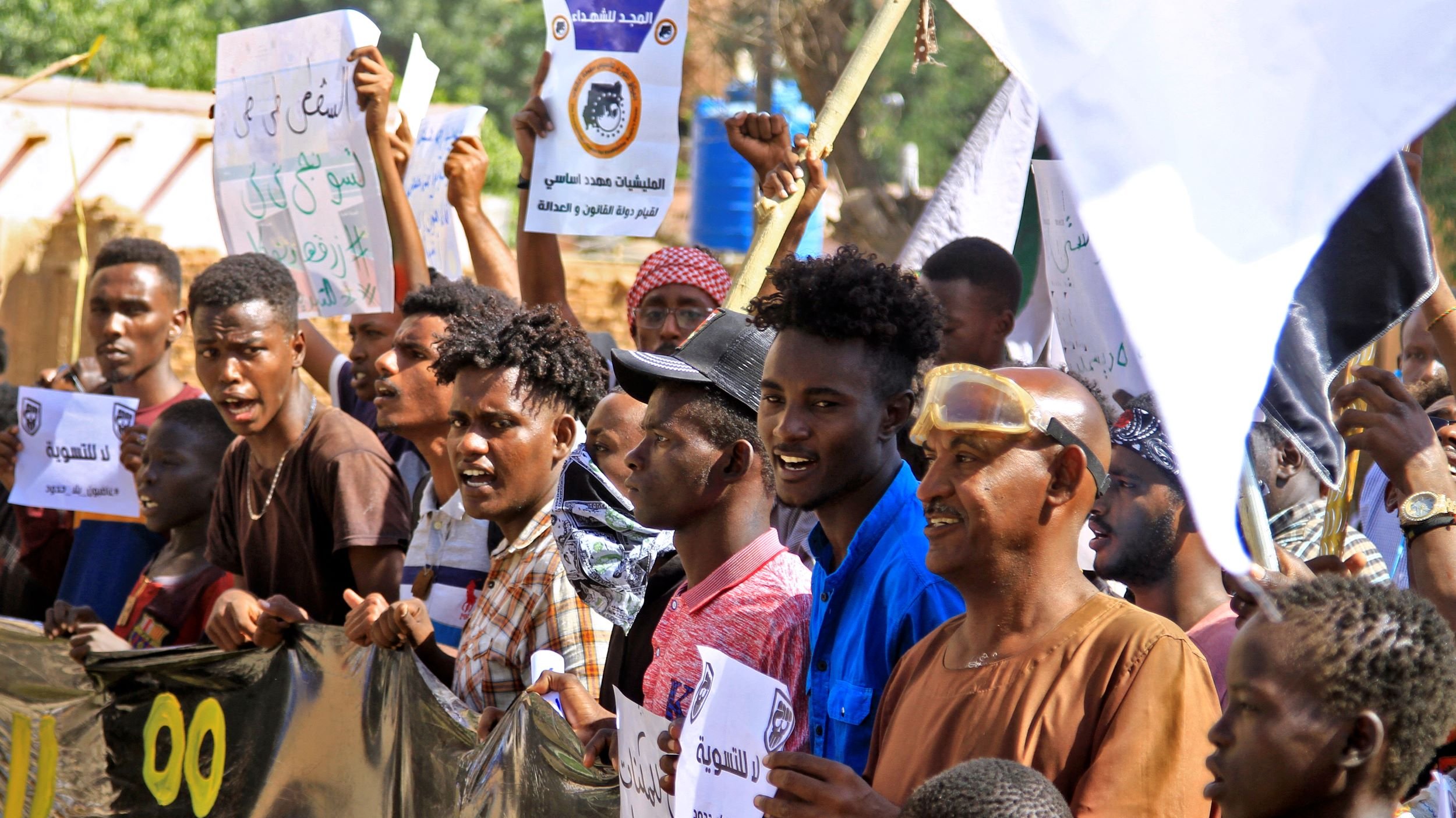در این تصویر گروهی از مردم در حال برگزاری تجمع یا تظاهرات هستند. آن‌ها پلاکاردهایی در دست دارند که روی آن‌ها نوشته‌هایی به زبان عربی وجود دارد. به نظر می‌رسد که این جمعیت شامل مردان جوان و بزرگسال است که برخی از آن‌ها لباس‌های سنتی و برخی لباس‌های عادی پوشیده‌اند. فضای تصویر نشان‌دهنده شور و هیجان جمعیت است و احتمالا این تظاهرات به یک مسئله اجتماعی یا سیاسی مرتبط است.