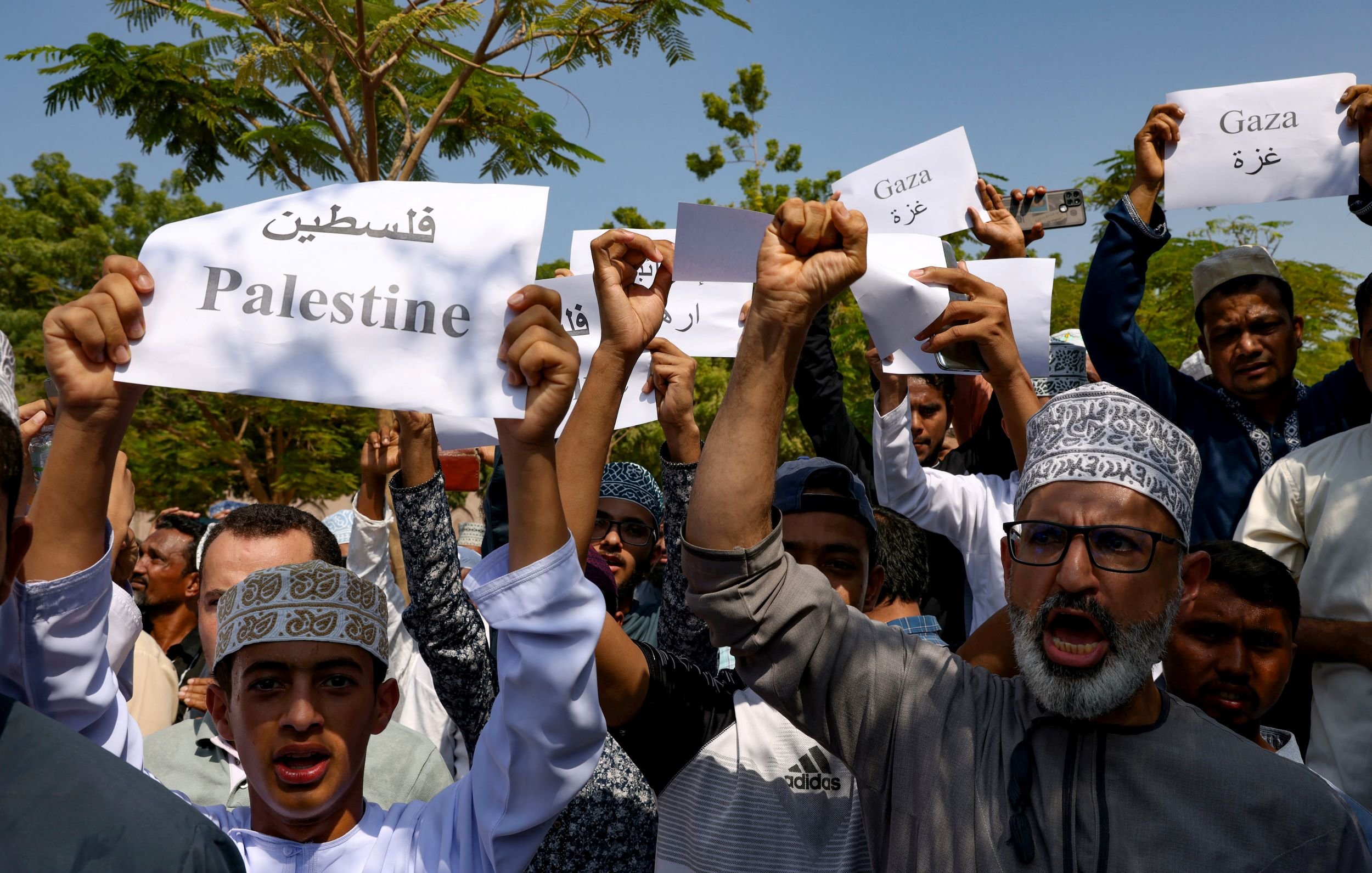 L'image montre un groupe de personnes tenant des pancartes en soutien à la Palestine et à Gaza. Les manifestants semblent rassembler pour exprimer leur solidarité, avec des expressions déterminées et des chants. Les pancartes affichent des mots en arabe ainsi qu'en anglais, reflétant un message de soutien à la cause palestinienne. L'environnement semble être en plein air, probablement lors d'une manifestation ou d'un rassemblement.