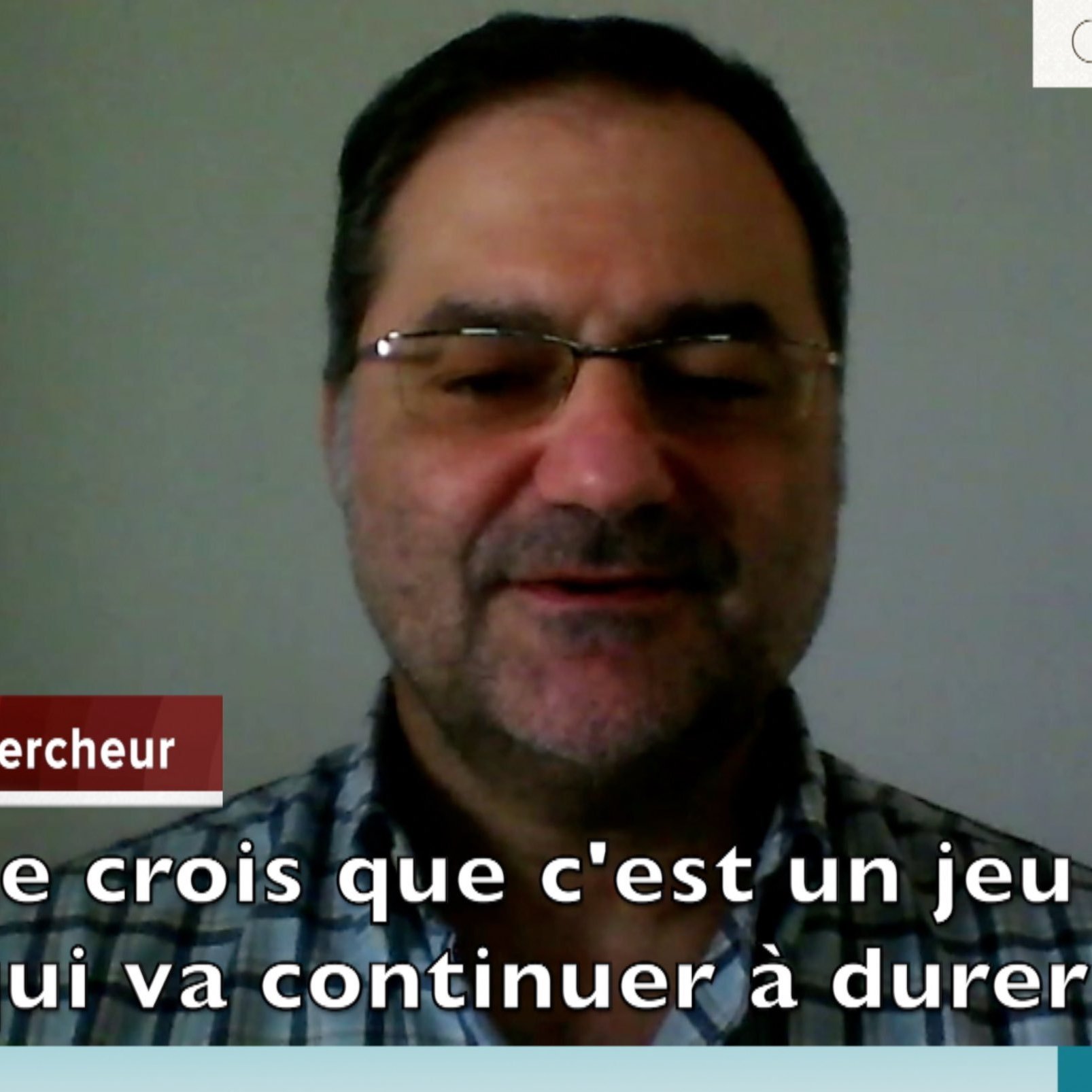 L'image montre un homme apparaissant en vidéoconférence. Il porte des lunettes et un chemisier à carreaux. Le texte en bas de l'image indique son nom, "Joseph Bahout, chercheur", suivi d'une citation où il exprime son opinion sur une situation, affirmant qu'il croit que "c'est un jeu qui va continuer à durer". Le fond est simple, et l'interface semble être d'une plateforme de communication vidéo.