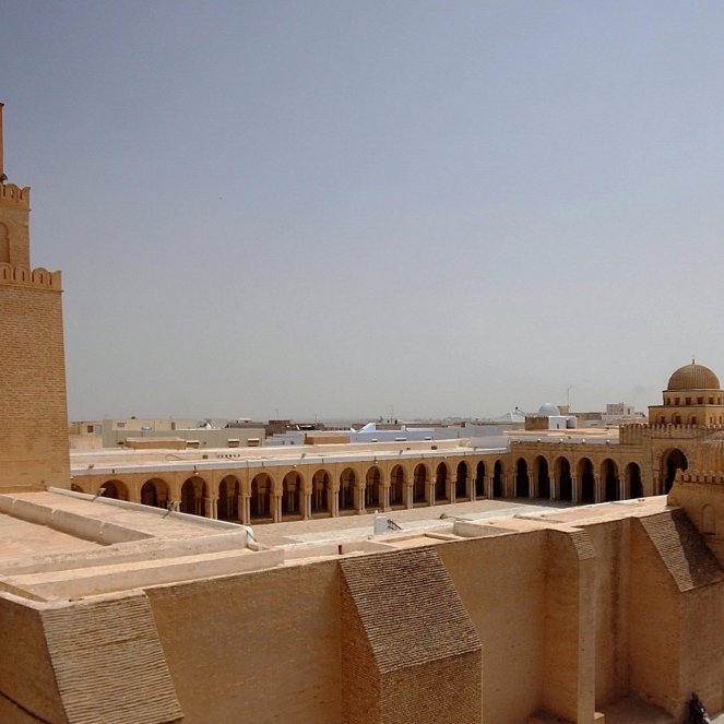 Edificio storico con torri e architettura in sabbia chiara, sole intenso.