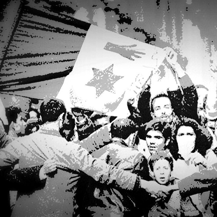 تظهر الصورة تجمعًا حاشدًا من الناس، يُرفع فيها علم يحمل نجمة. يظهر الحماس والتضامن بين المشاركين، حيث يتداخلون ويعبرون عن مشاعر قوية من الإصرار. تعكس الصورة لحظة من التاريخ، حيث تتجلى فيها روح الوحدة والتغيير. الخلفية تبدو غامقة، مما يضيف بعدًا دراماتيكيًا للصورة.