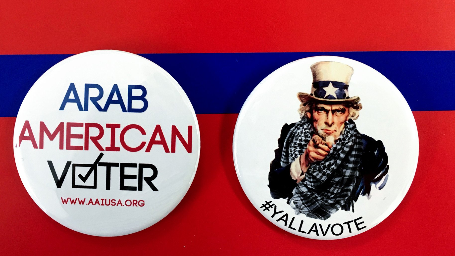 L'image montre deux badges sur un fond rouge avec une bande bleue. Le premier badge mentionne "ARAB AMERICAN VOTER" avec un symbole de coche, tandis que le deuxième badge représente un personnage qui ressemble à l'oncle Sam, avec le texte "#YALLAVOTE". Ces badges mettent en avant l'importance du vote et de l'engagement civique, en particulier au sein de la communauté arabe-américaine.